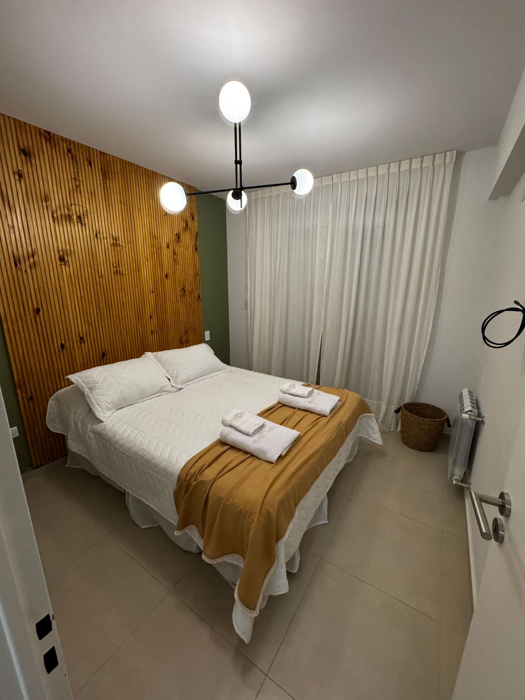 Dormitorio con respaldo de madera, cama doble y toallas bordadas