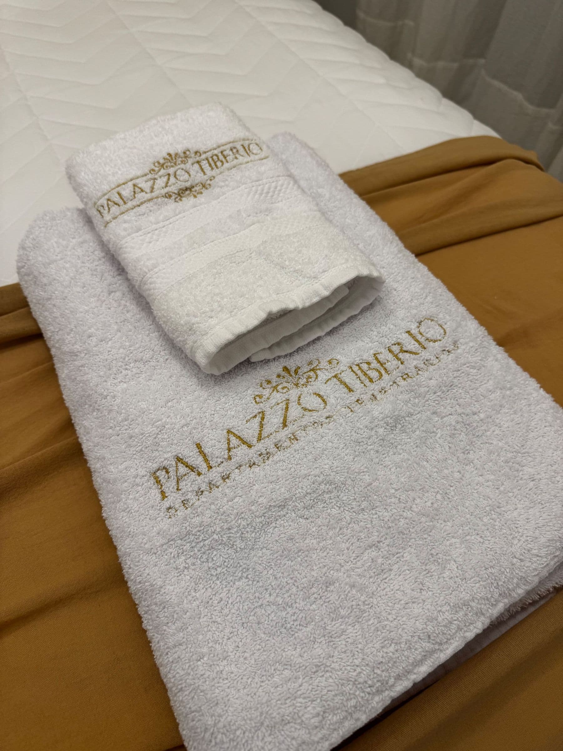 Toalla bordada con el logo de Palazzo Tiberio sobre la cama