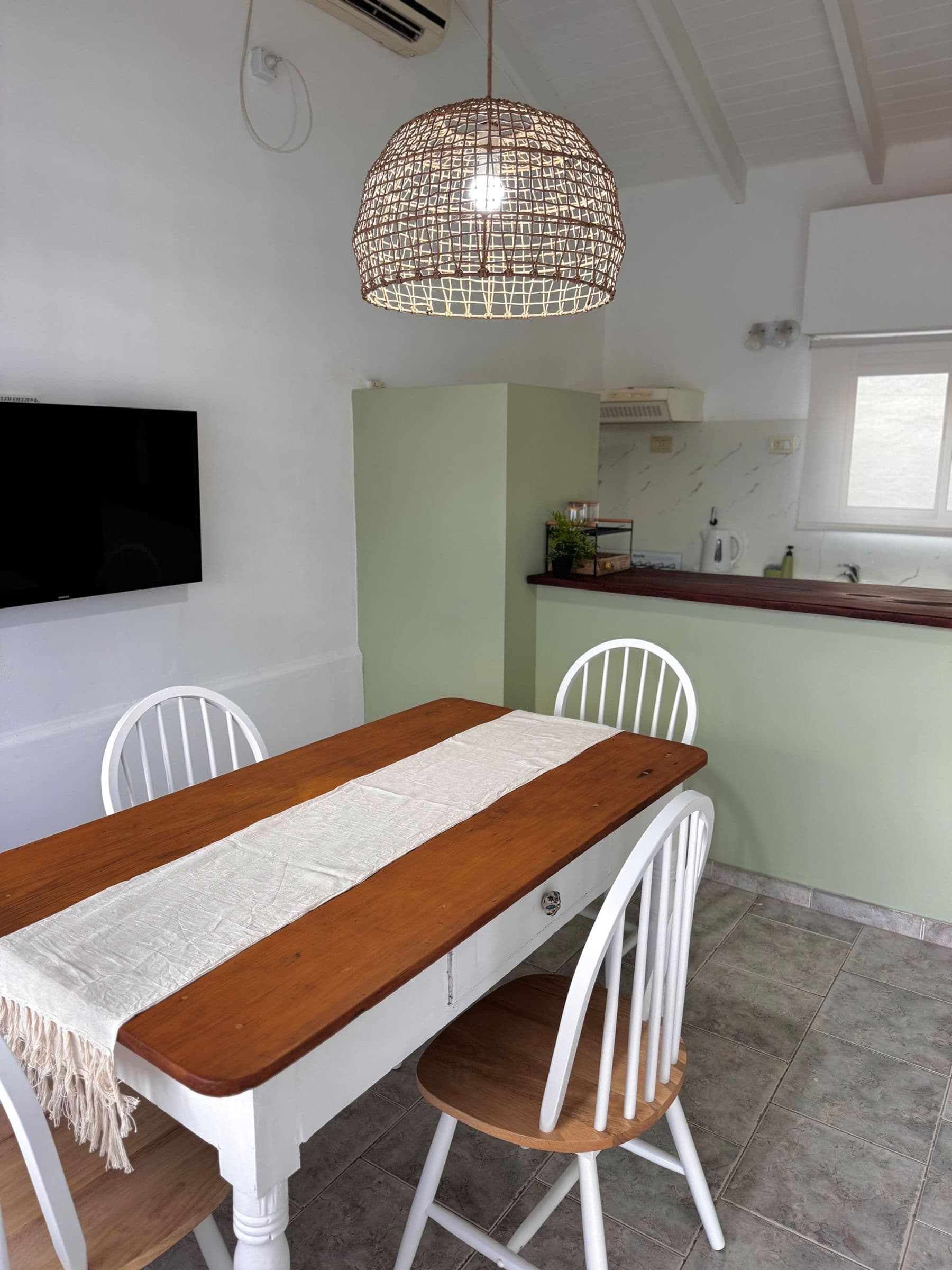 Mesa de comedor blanca y madera con sillas, cocina verde al fondo