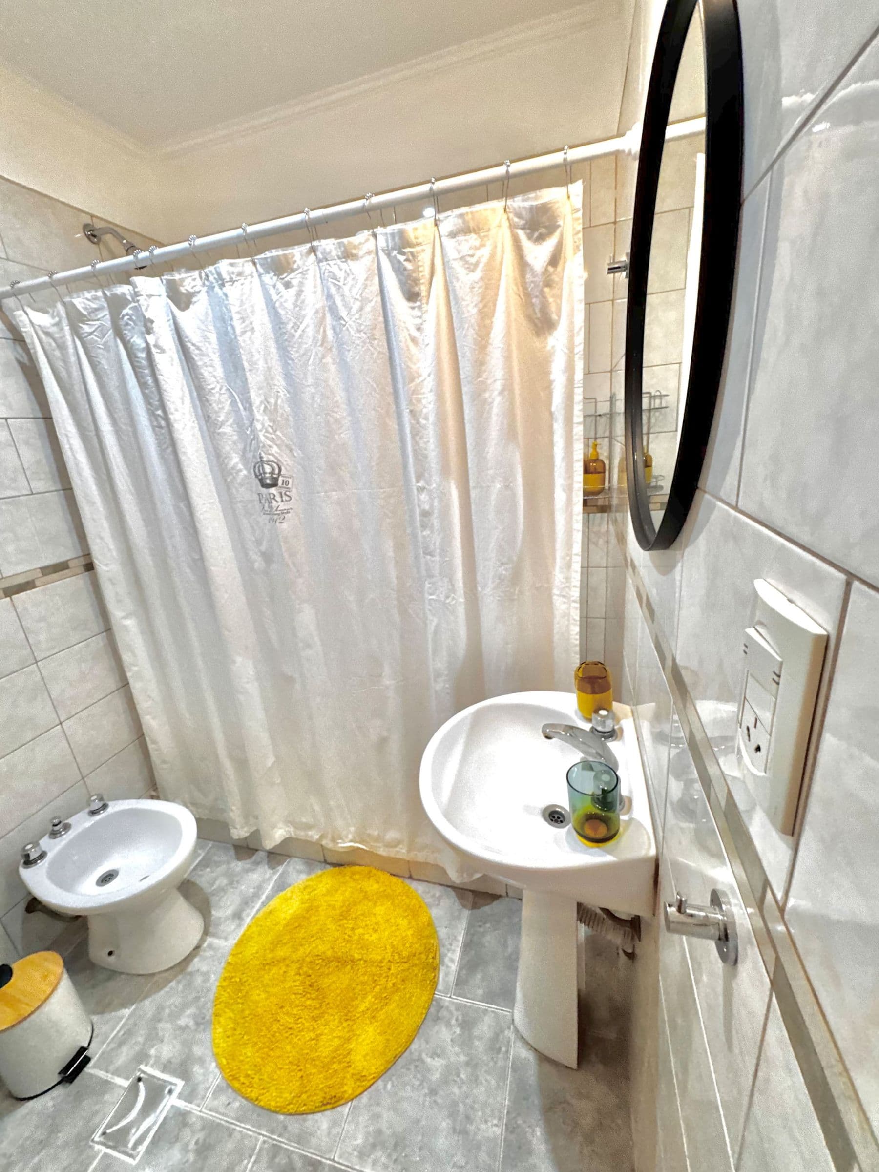 Baño con bidet, espejo redondo y cortina de ducha